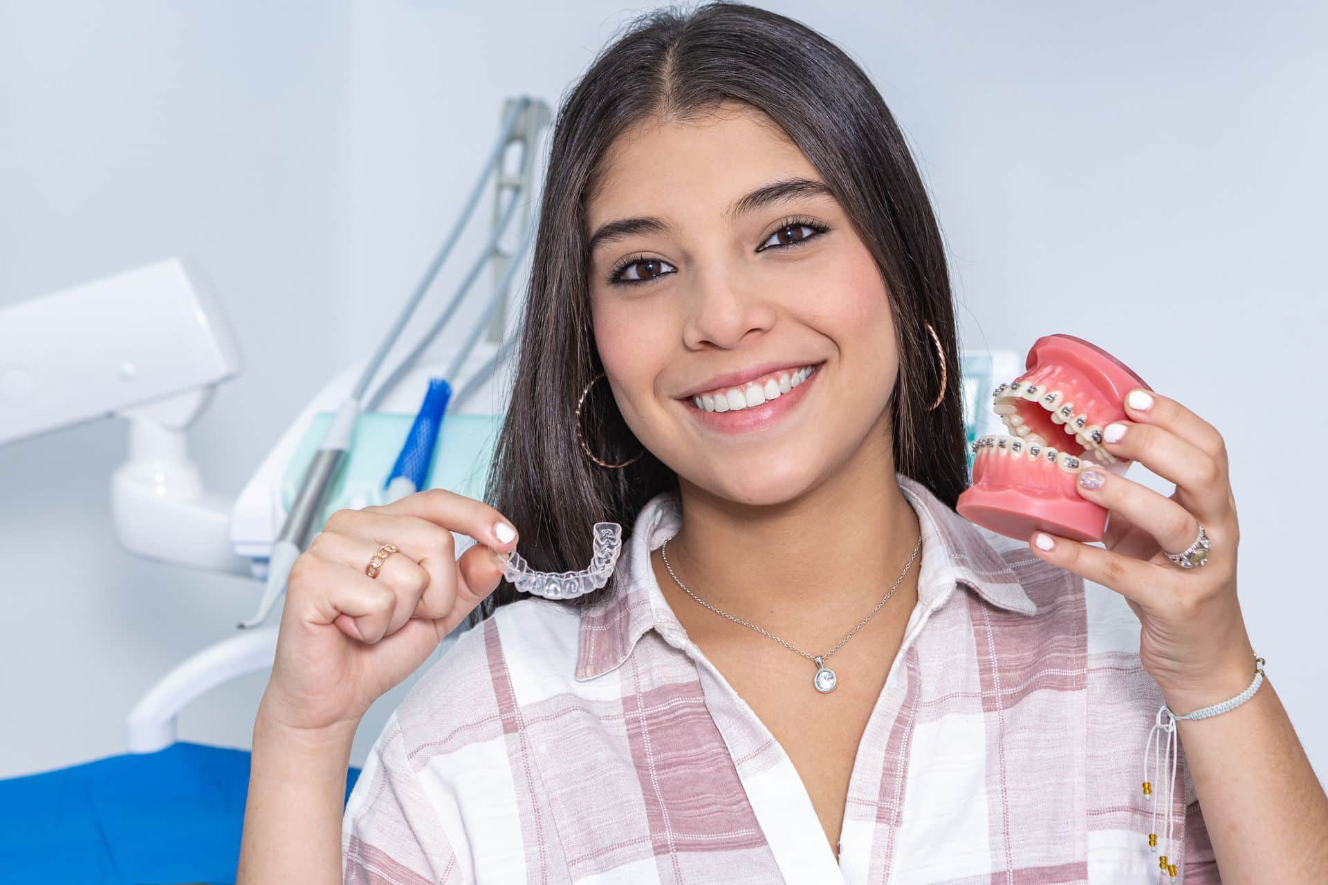 Smiling young woman holding a clear aligner and a dental model with braces