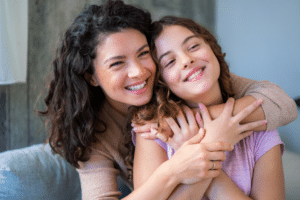 Mother and young daughter with healthy smiles hugging closely indoors